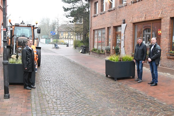 Bauamtsleiter Roland Klewwe (links), Bauamtsmitarbeiter Patric Fuhrhop (2. von rechts) und Bürgermeister Martin Feller stehen an der Zufahrt zur Lüneburger Straße, an der zwei Blumenkübel den Verkehr ausbremsen sollen. 